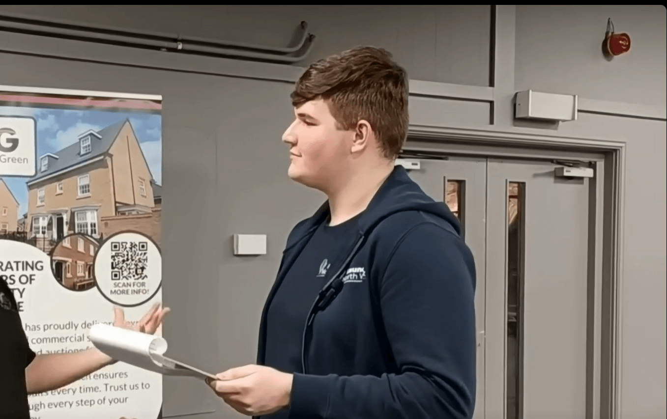 Launch North West marketing apprentice Oliver speaking with an exhibitor at a business event while holding a notepad, with exhibition stands in the background.