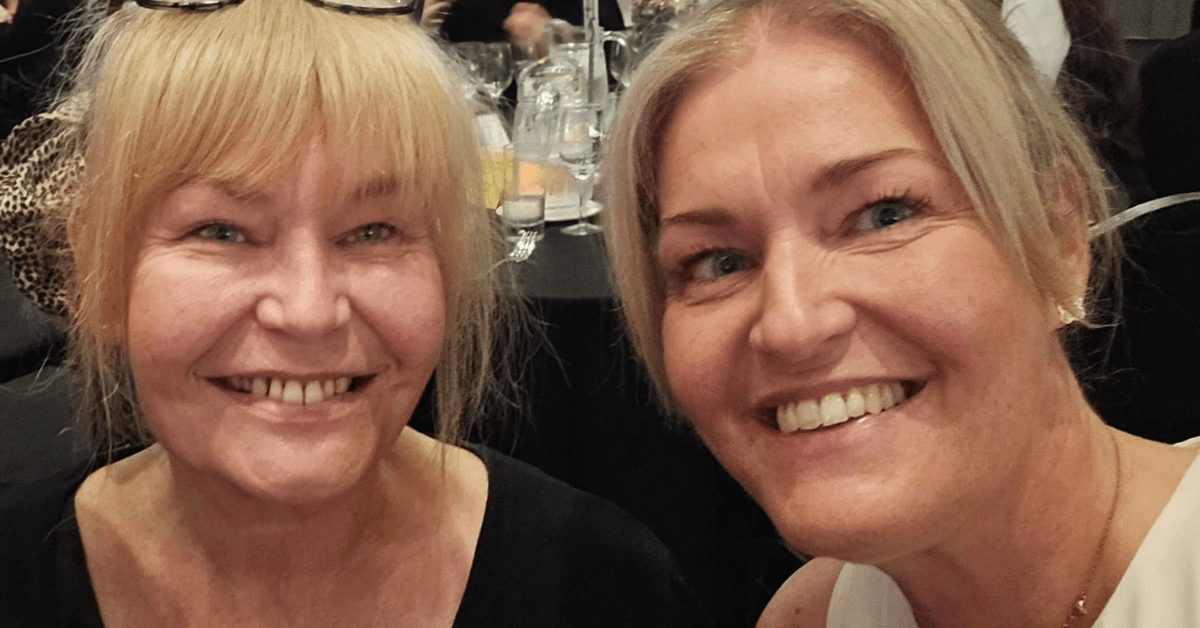 Two smiling women posing together at an awards dinner. They are seated among other guests and tables at the Excellence Awards 2026 event.